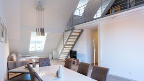 Een ruime woonkamer met een hoge plafond, een eettafel en een trap naar een hoger niveau.