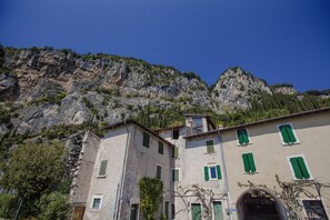 A building with multiple windows and a stone facade, set against a mountainous backdrop. - Pomelo Apartment (tignale)