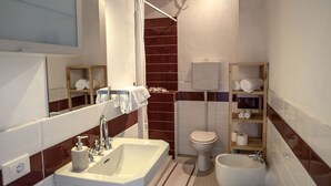 Un bagno con soffitto in legno, un lavandino, un water e un bidet. Asciugamani e un cesto sono presenti sul pavimento.