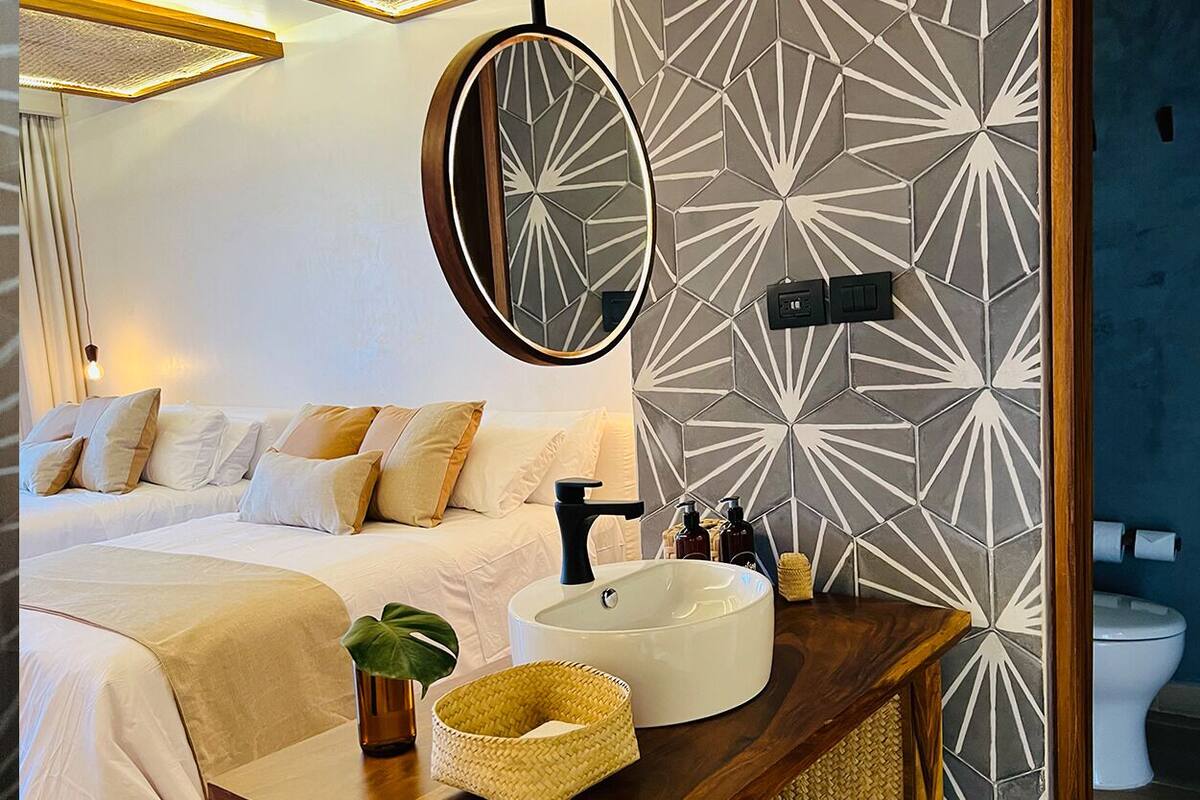 A bedroom with a bed, bedside table, mirror, and a bathroom with a toilet and sink.