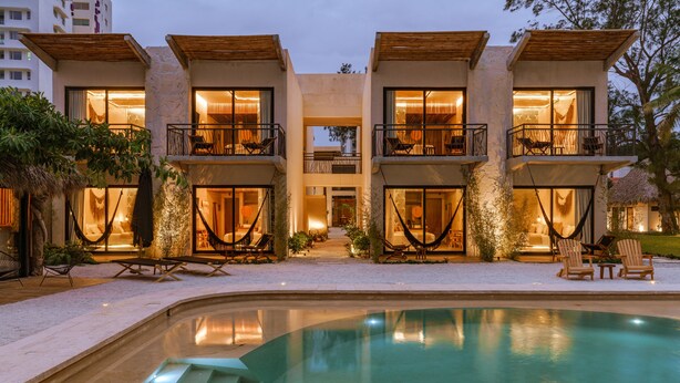 A modern two-story building with a swimming pool, outdoor seating, and a well-lit entrance.