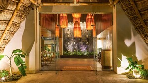 A thatched-roof structure with a glass entrance, indoor plants, and hanging lights.