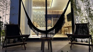 A modern patio with a hammock, two wooden chairs, and a small table.