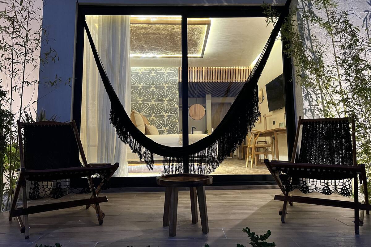 A modern patio with a hammock, two wooden chairs, and a small table.