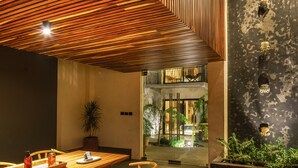 A modern interior with a wooden slatted ceiling, a dining area with a table and chairs, and a view of the outside through a glass door.