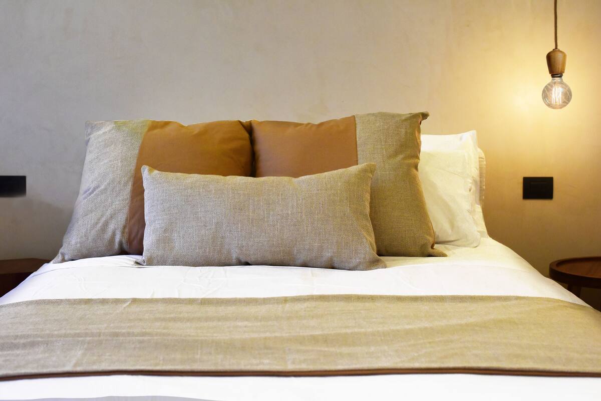 A neatly made bed with multiple pillows and a light fixture above.