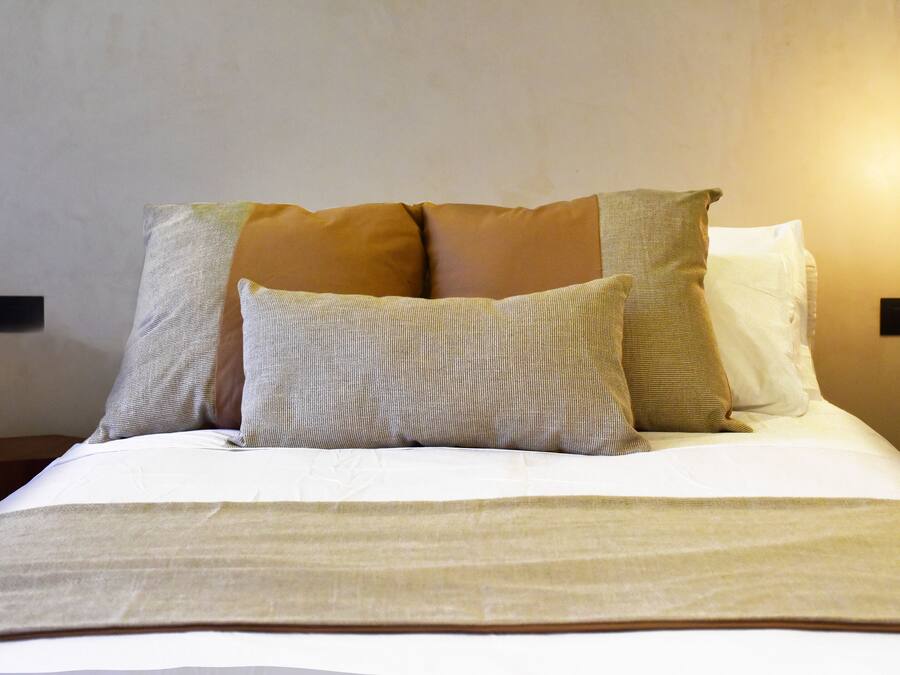 Una cama bien hecha con varias almohadas y una lámpara colgante arriba.