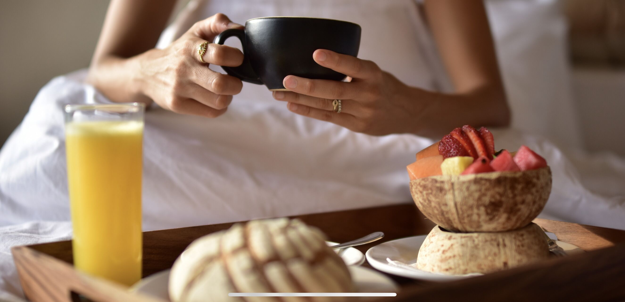 A person holding a black mug, a glass of orange juice, and a plate with a bowl of fruit and a tortilla.