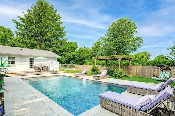 A backyard with a swimming pool, lounge chairs, a pergola, and a wooden fence.