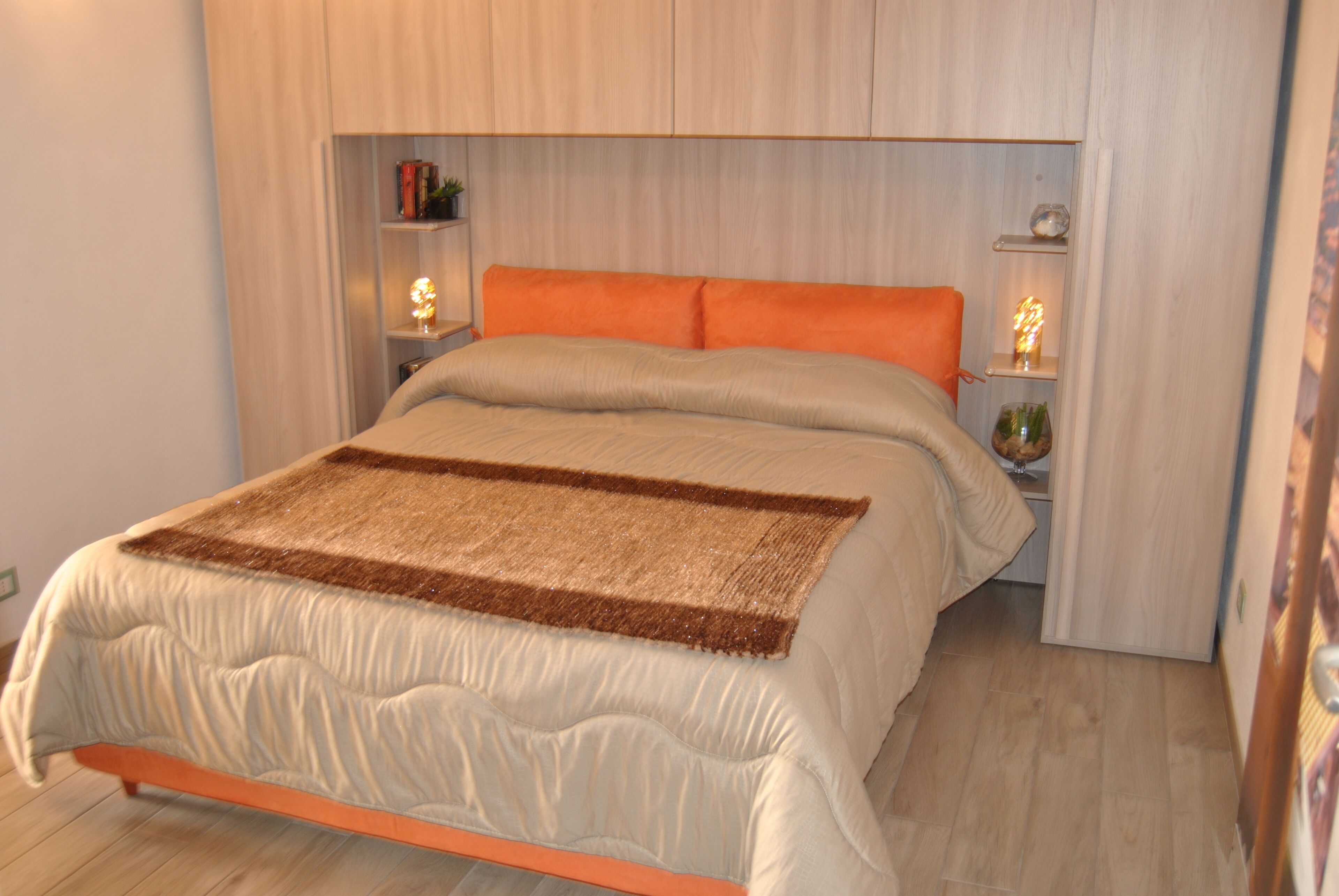 A neatly made bed with a brown throw, a wooden headboard, and bedside tables with lamps.