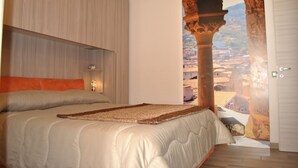 Une chambre à coucher avec un lit, une table de chevet et une vue sur le paysage urbain, visible à travers une porte ouverte.