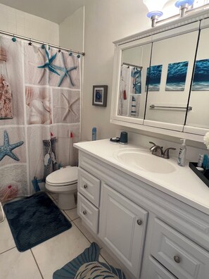 A bathroom with a white sink, a mirror, and a toilet. There is a shower curtain with starfish and coral designs. - This Gorgeous Oceanview Condo is the Perfect Caribbean Retreat! (Christiansted)