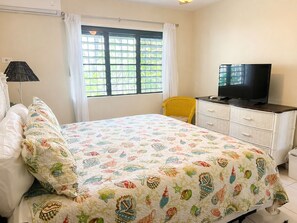 Ein Schlafzimmer mit einem Bett, einem Fernseher auf einer Kommode, einem Fenster mit Vorhängen und einem Sessel.