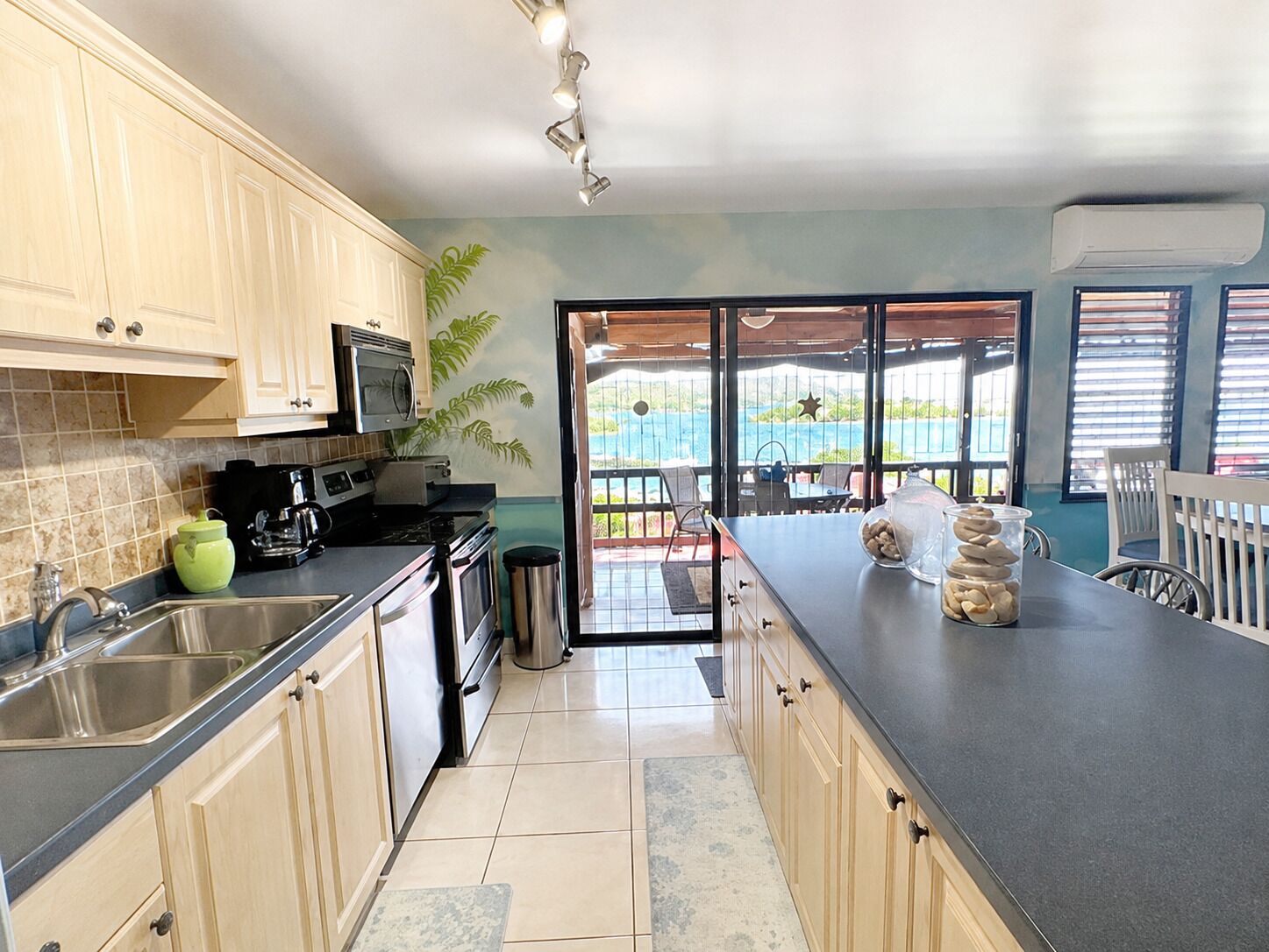 A kitchen with a view to a balcony, a sink, a stove, and a countertop with a jar of stones.