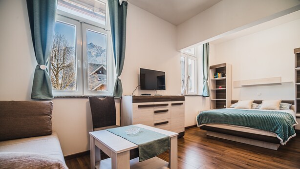 Een moderne slaapkamer met een bed, een bureau, een televisie en een raam met gordijnen.