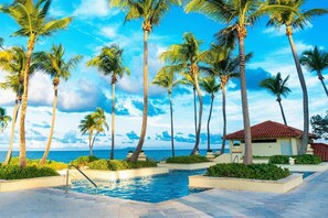 A pool area with palm trees and a view of the ocean. - Marbella at Palmas del Mar Outstanding Condo (Humacao)