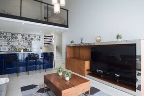 A modern kitchen with blue bar stools, a wooden dining table, and a large flat-screen TV. - Beach Villages, 3 Bedrooms, Just Renovated (Humacao)