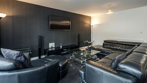 A modern living room with a glass coffee table, leather sofas, and a flat-screen TV mounted on the wall. - Beautiful 3-bed Apartment in Romford (Romford)