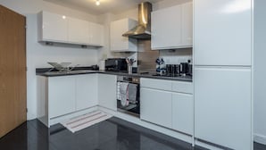 A modern kitchen with white cabinets, a stainless steel range hood, a built-in oven, and a coffee machine. - Beautiful 3-bed Apartment in Romford (Romford)