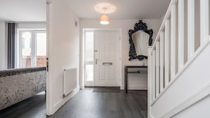 A hallway with a white door, a black-framed mirror, and a light fixture. - Beautiful 3-bed Apartment in Romford (Romford)
