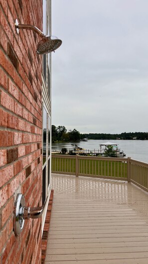 Une terrasse en bois avec une rambarde en métal, un mur de briques et une vue sur un lac où naviguent des bateaux.