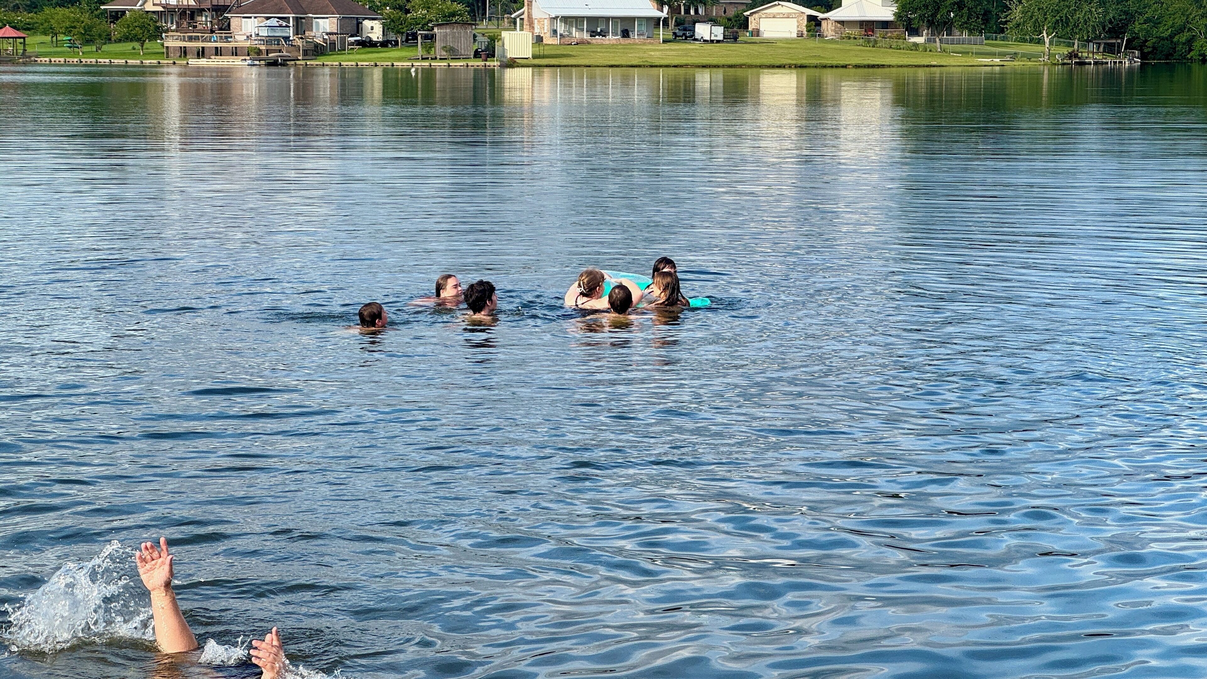Um grupo de pessoas nadando em um lago, com casas ao fundo.