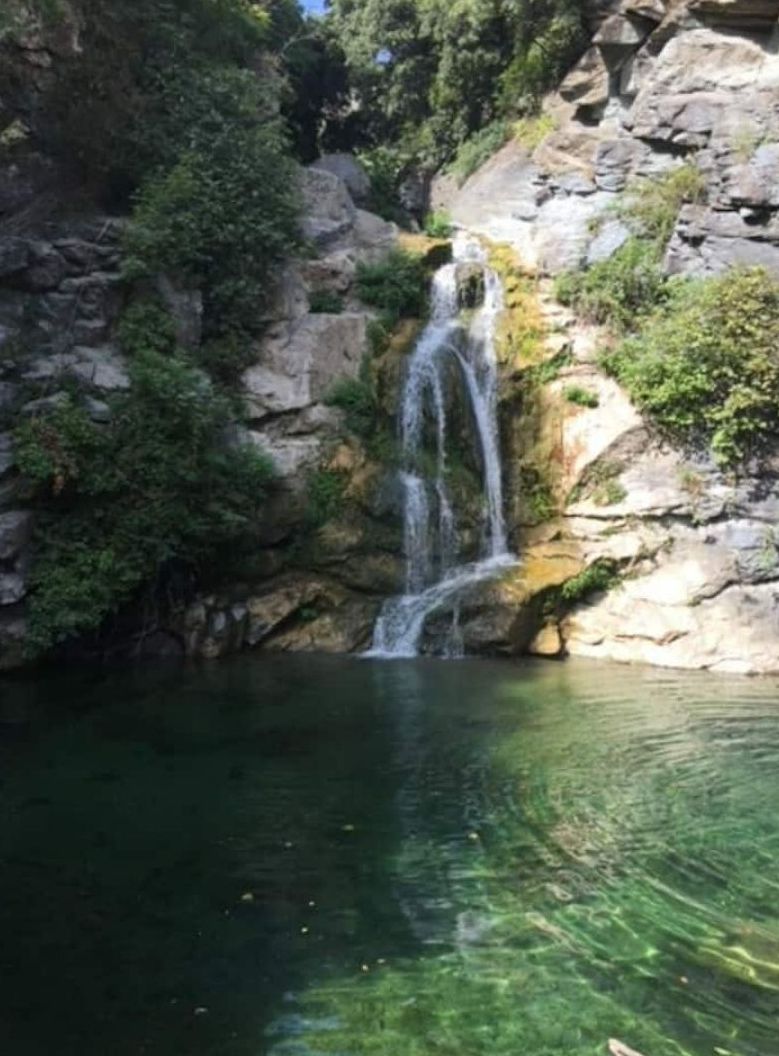 Une cascade se jetant dans un bassin d’eau claire, entouré d’un paysage rocheux et de verdure.