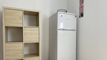 A white refrigerator with a freezer on top, a wooden cabinet with multiple compartments, and a wall-mounted picture frame with a floral design.