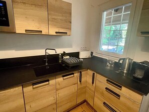 A kitchen with wooden cabinets, a black countertop, a coffee machine, and a kettle. - Central Cap Ferret location, all on foot A0342 (Cap Ferret)