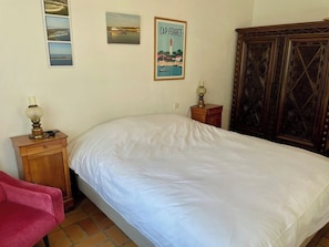 A bedroom with a bed, a nightstand, a lamp, a wooden wardrobe, and a poster on the wall. - Central Cap Ferret location, all on foot A0342 (Cap Ferret)