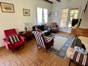 A living room with a red armchair, striped armchairs, a sofa, a coffee table, and a television. - Central Cap Ferret location, all on foot A0342 (Cap Ferret)