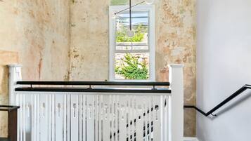 A staircase with a white railing, a view of greenery outside through a window, and a textured wall.