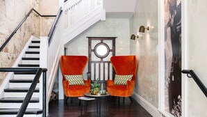 A staircase with a white railing leading to a landing. There are two orange armchairs with patterned cushions, a small round table with a plant and a tray, and a framed picture on the wall. - Terminus Pyrmont (Pyrmont)