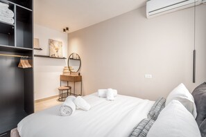 A hotel room with a neatly made bed, a wardrobe, a mirror, and a small table with towels.