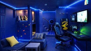 A room with a climbing wall, a gaming chair, a desk with a computer, and a TV.