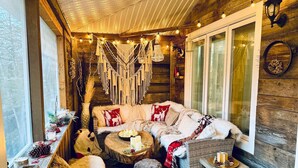 A cozy cabin interior with a sofa set, a round wooden table, and a window with curtains.