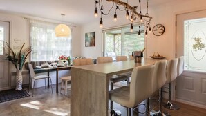 A modern kitchen with a central island, pendant lighting, and a dining area with a view of the outdoors.