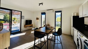 Une cuisine moderne avec un coin repas, de grandes fenêtres et une vue sur l’extérieur.
