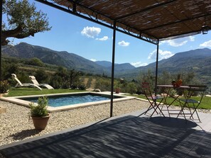 Un espace piscine avec des chaises longues, une table garnie de fruits et une vue sur les montagnes.