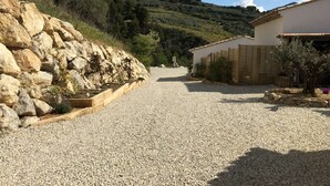 Une allée de gravier mène à un bâtiment, avec un mur de soutènement en pierre sur le côté gauche.