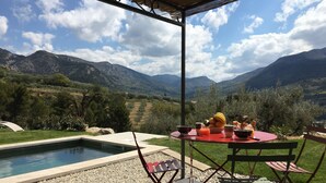 Un espace repas aménagé au bord de la piscine, avec une table dressée pour deux personnes, offrant une vue sur un paysage montagneux.