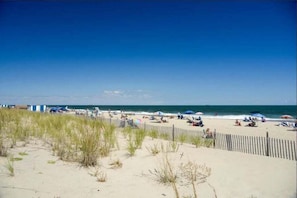 Une plage avec une clôture en bois, des dunes de sable et des parasols.