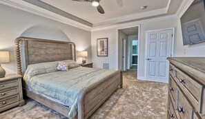 Ein Schlafzimmer mit einem Bett, Nachttischen, einer Kommode, einem Deckenventilator und einer Tür zu einem anderen Raum.