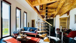 Amplia sala de estar con un sofá azul, un tapete rojo, una escalera de madera y una zona de comedor con sillas rojas.