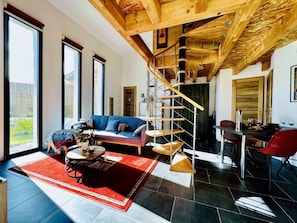 A spacious living area with a blue sofa, a red rug, a wooden staircase, and a dining area with red chairs.