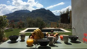 Una mesa de desayuno con frutas, un vaso de zumo de naranja y vistas a las montañas.