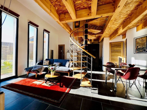 A spacious living area with a wooden ceiling, a blue sofa, a dining table with red chairs, and a spiral staircase. - ⭐ Le Grand Sabouillon ⭐ Loft-style villa ⭐ private pool ⭐ Mont Ventoux view ⭐ (Buis-les-Baronnies)