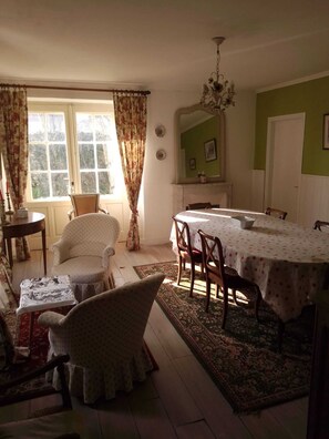 A dining area with a table set for four, surrounded by chairs, a chandelier, and a large window with curtains.