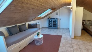 Une chambre à coucher aménagée dans un espace mansardé, avec un plafond en pente, un canapé-lit, une petite table d’appoint et un meuble de rangement.