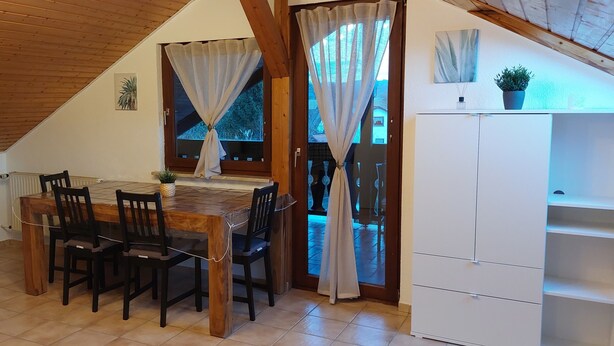 Un coin repas avec une table et des chaises en bois, un téléviseur posé sur un meuble et un buffet blanc.